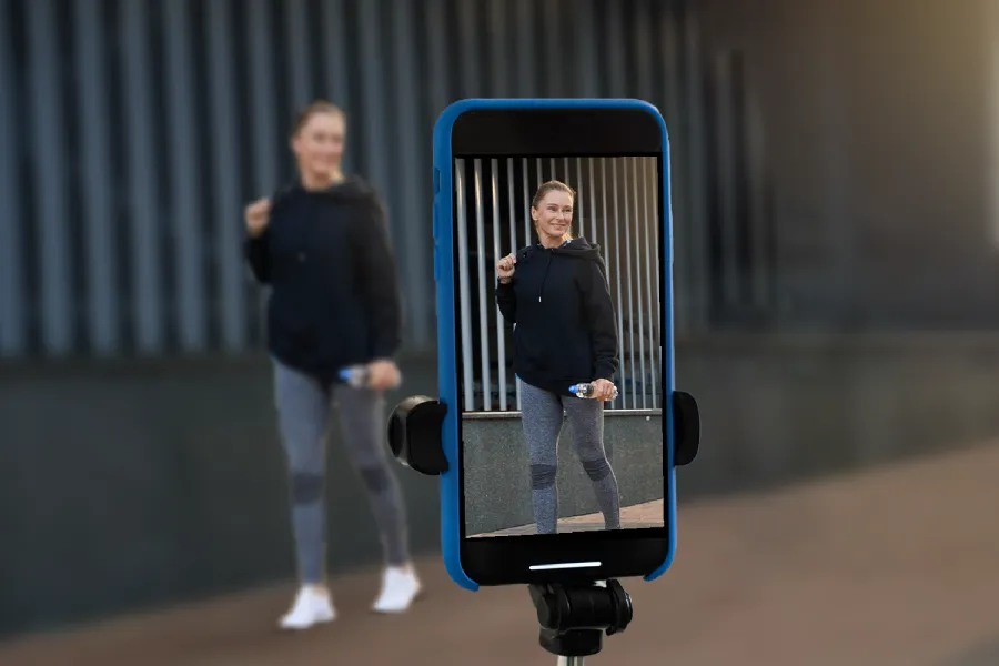 A cellphone filming a young woman is in the foreground, while the full scene is visible (and blurry) in the background. .