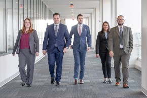Five Patent Trials and Appeal Board judicial law clerks walking side by side down a hall corridor. caption: Five PTAB judicial law clerks walking side by side down a hall corridor.
